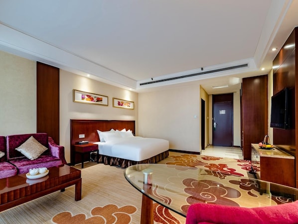 A hotel room with a bed, a sofa, a glass coffee table, a TV, and a door leading to another room. - Madison Hotel Tai Mountain Scenic Spot (Tai'an)