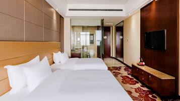 A hotel room with two beds, a TV, a bathroom, and a hallway leading to other rooms.