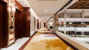 Pasillo de hotel con puertas de madera, alfombra estampada y vista del nivel inferior a través de una barandilla de cristal.