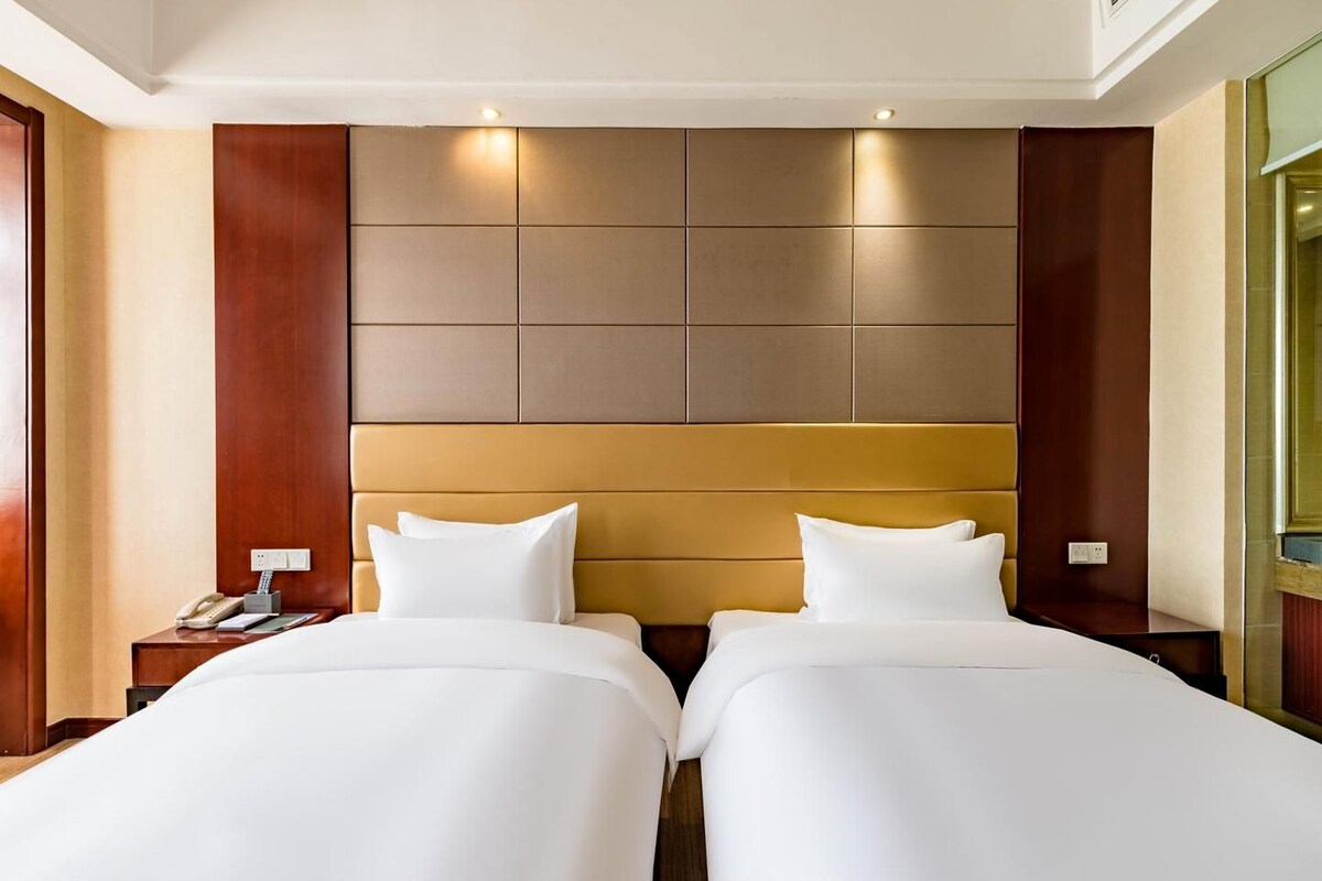 A hotel room with two beds, a wooden headboard, a bedside table with a phone, and a wall-mounted light.
