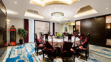Un comedor con una mesa redonda, sillas rojas, una araña y una planta grande en maceta.
