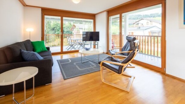 A spacious living room with a sofa, a TV, a chair, and a balcony with a view. - Casa Miro Nr. 7 by Interhome (Flims)