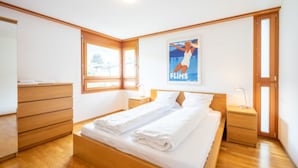 A bedroom with a wooden bed, a nightstand, a dresser, and a poster on the wall. - Casa Miro Nr. 7 by Interhome (Flims)