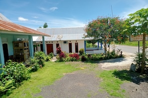 A building with a corrugated metal roof, a signboard, and a well-maintained garden with various plants and flowers. - OYO 91230 Kelimutu Eco Village (Moni)