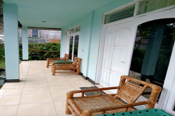 A covered outdoor area with tiled flooring, wooden chairs, and a white door. - OYO 91230 Kelimutu Eco Village (Moni)