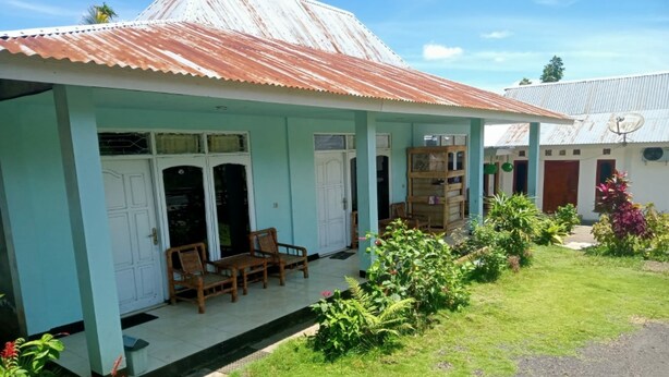 A two-story building with a corrugated metal roof, a covered porch with chairs, and a garden area. - OYO 91230 Kelimutu Eco Village (Moni)
