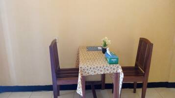 Une petite pièce avec une table recouverte d’une nappe à motifs floraux, deux chaises en bois, un vase avec des fleurs et une boîte étiquetée « PASEO ».