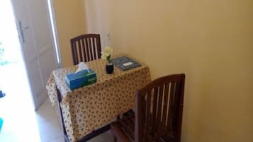 Un comedor con una mesa cubierta con mantel floral, dos sillas de madera, un jarrón con flores y una caja de pañuelos.