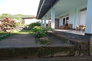 A covered outdoor area with a concrete pathway, wooden chairs, and a motorcycle. - OYO 91230 Kelimutu Eco Village (Moni)