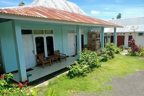 A two-story building with a corrugated metal roof, a covered porch with chairs, and a garden area. - OYO 91230 Kelimutu Eco Village (Moni)