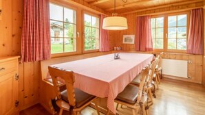 Una habitación con paneles de madera, una mesa larga, sillas y ventanas amplias.