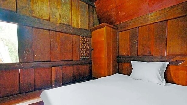 A wooden room with a bed, a window, and a wall with a decorative panel.