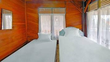 A room with wooden walls, two beds with white bedding, a window with curtains, and a small mirror on the wall.