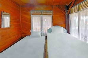 Una habitación con paredes de madera, dos camas con ropa blanca, una ventana con cortinas y un espejo pequeño en la pared.