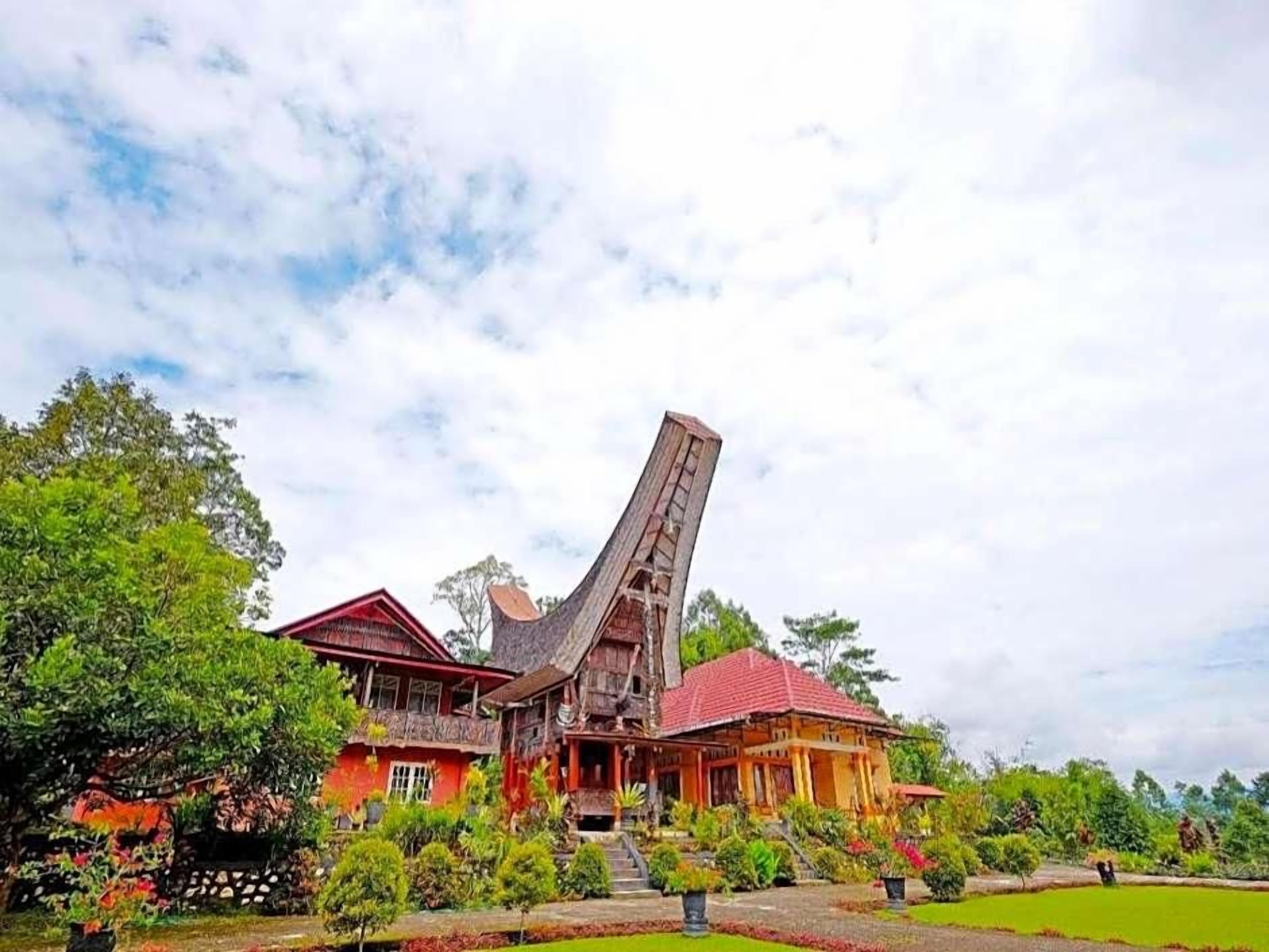 A traditional wooden house with a steeply pitched roof, surrounded by lush greenery and a well-maintained garden.