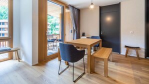 Ein modernes Zimmer mit Holzboden, einem Tisch mit Stühlen, einer Bank, einer Tür und Blick durch eine Glastür in einen Außenbereich.