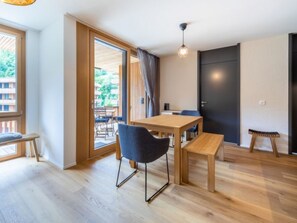 A modern room with a wooden floor, a table with chairs, a bench, a door, and a view through a glass door to an outdoor area. - Vallada 14_01 by Interhome (Flims)