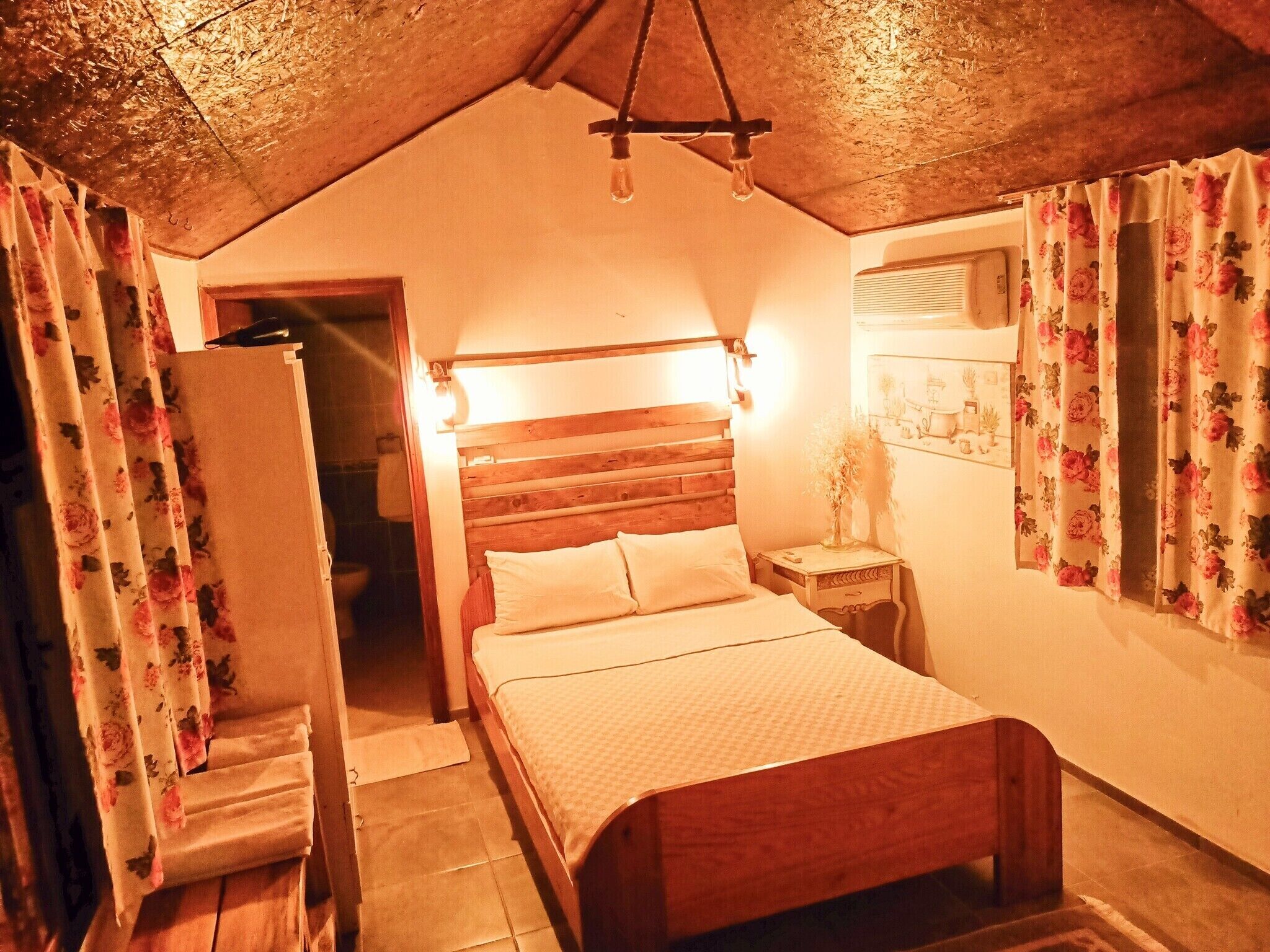 A bedroom with a wooden bed, a nightstand, a hanging light fixture, and floral curtains.
