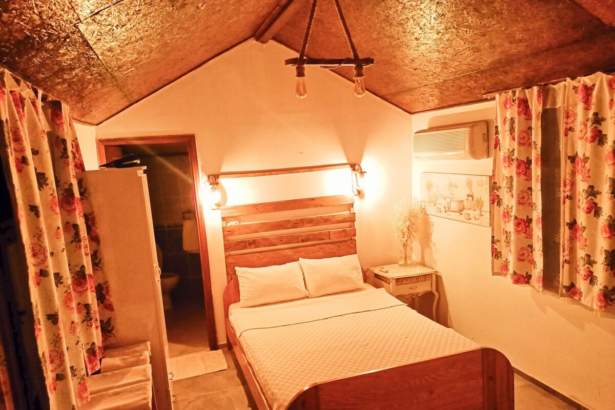 Un dormitorio con una cama de madera, una mesita de noche, una lámpara colgante y cortinas con motivos florales.