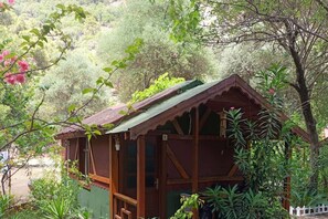 Una cabaña de madera con techo inclinado, rodeada de exuberante vegetación y árboles.