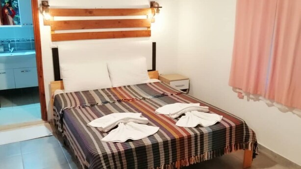 A bedroom with a wooden headboard, a striped bedspread, and two towels on the bed. - Canario Bungalows (Kemer)