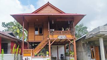 A two-story wooden house with a balcony, a sign reading 'Juniper Home Sweet,' and various potted plants.