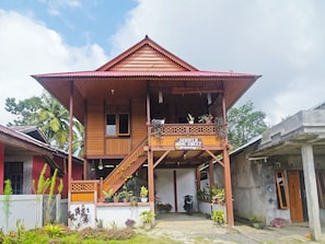 A two-story wooden house with a balcony, a sign reading 'Juniper Home Sweet,' and various potted plants. - OYO 91246 Pulisan Ekowisata Homestay (Manado)