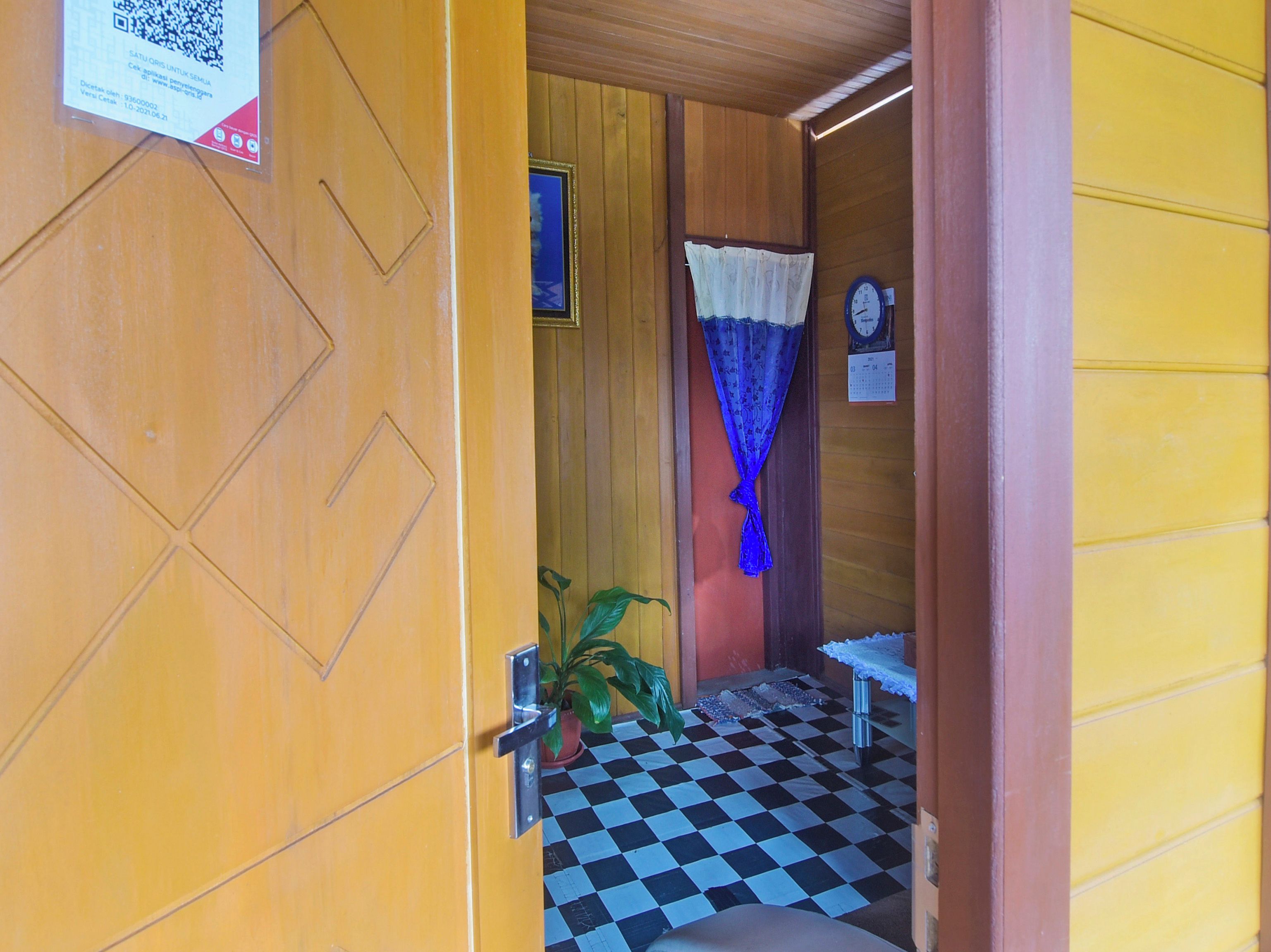 A room with a checkered floor, a wooden door, a potted plant, a blue curtain, and a wall clock.