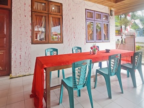A dining area with a red tablecloth, wooden chairs, and a window with curtains. - OYO 91246 Pulisan Ekowisata Homestay (Manado)