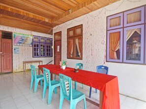 Un'area pranzo con un lungo tavolo rosso, sedie blu e un soffitto in legno.