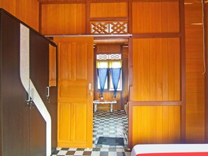 Una stanza con pareti in legno, pavimento a scacchi, un letto e una porta che conduce a un'altra stanza.
