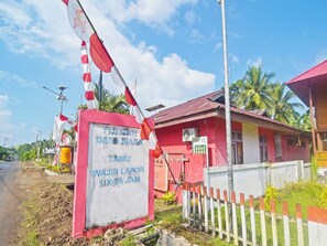 A signboard with text, a red building, a white fence, and a street. - OYO 91246 Pulisan Ekowisata Homestay (Manado)