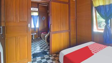 A room with a checkered floor, wooden walls, a bed with a red and white bedspread, a window with blue curtains, and a door leading to another room.