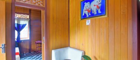 A wooden interior with a checkered floor, a white chair, a potted plant, and a framed picture of two white cats.