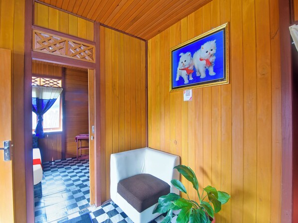 A wooden interior with a checkered floor, a white chair, a potted plant, and a framed picture of two white cats. - OYO 91246 Pulisan Ekowisata Homestay (Manado)