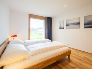 Ein modernes Schlafzimmer mit einem Holzbett, einem großen Fenster und zwei Landschaftsbildern an der Wand.