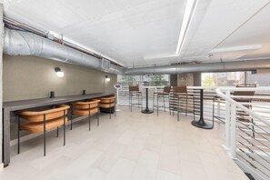 Un espace bar moderne avec des tabourets hauts, un long comptoir et une vue sur la ville grâce à de grandes fenêtres.