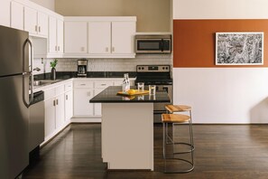 Una cocina moderna con armarios blancos, electrodomésticos de acero inoxidable, una isla con encimera negra y un taburete de bar.