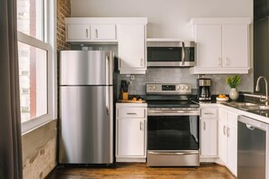 A modern kitchen with stainless steel appliances, white cabinetry, and a brick wall. - Reside Houston Downtown A Wyndham Residence (Houston)