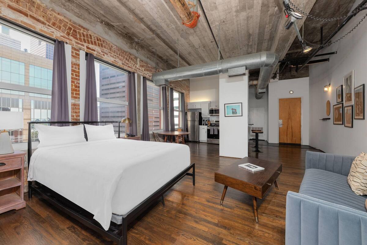 Ein modernes Hotelzimmer mit einem großen Bett, Holzboden, einer Küchenzeile und Blick auf die Stadt.