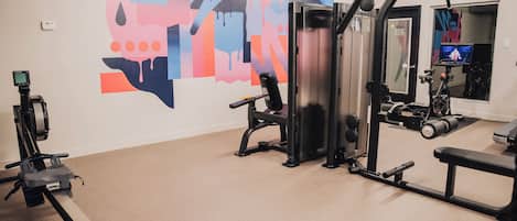 Een sportschool met trainingsapparatuur, een muur met abstracte kunst en een spiegel.