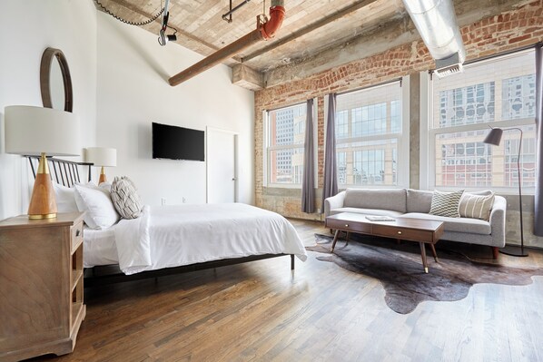 Ein modernes Schlafzimmer mit Bett, Sofa und einem großen Fenster.