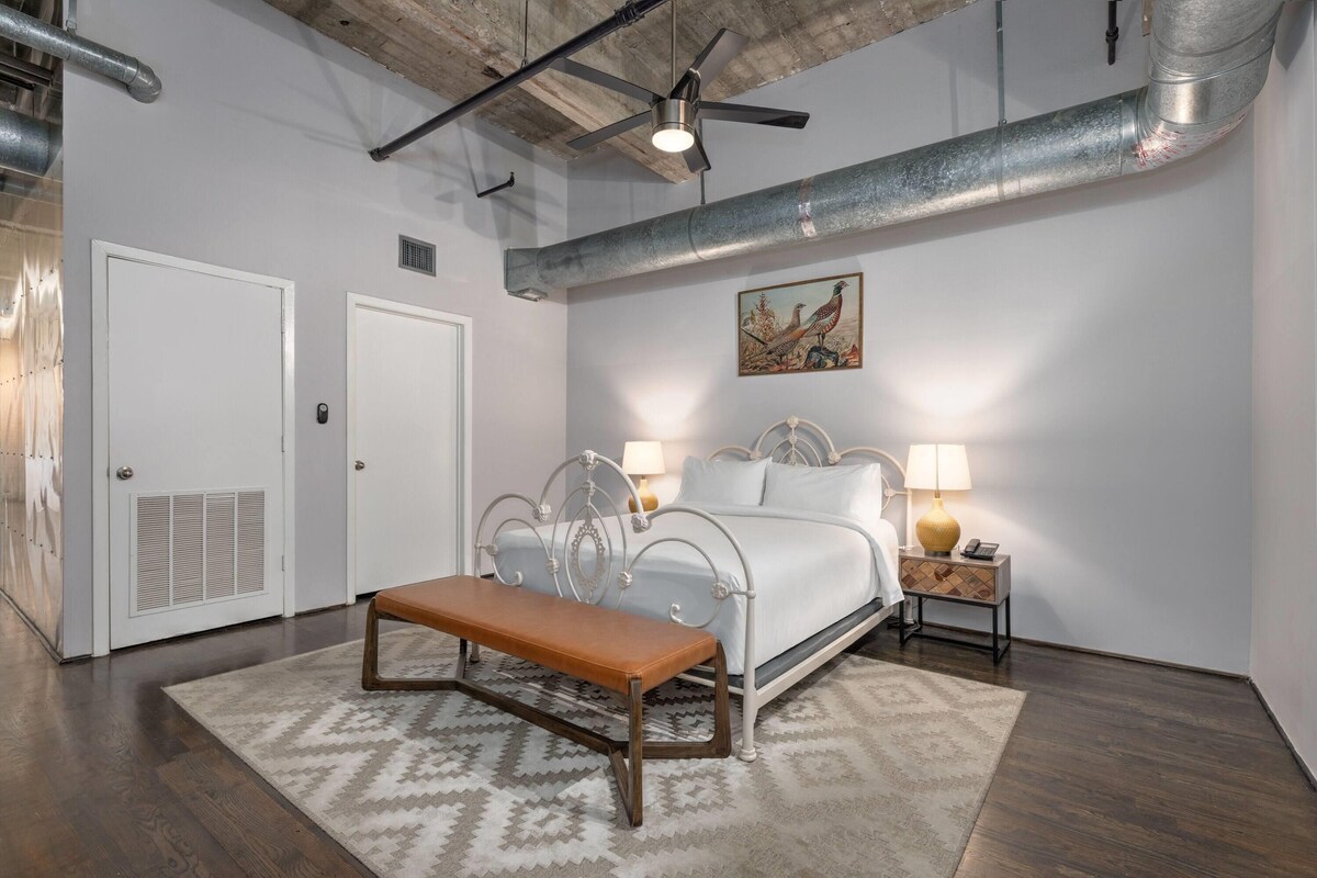 A bedroom with a bed, a bench, a nightstand, a lamp, and a painting on the wall.