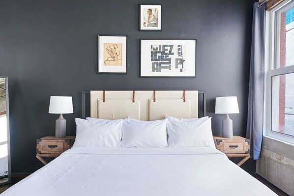 Una cama con ropa blanca, dos mesitas de noche con lámparas y una obra de arte en la pared.