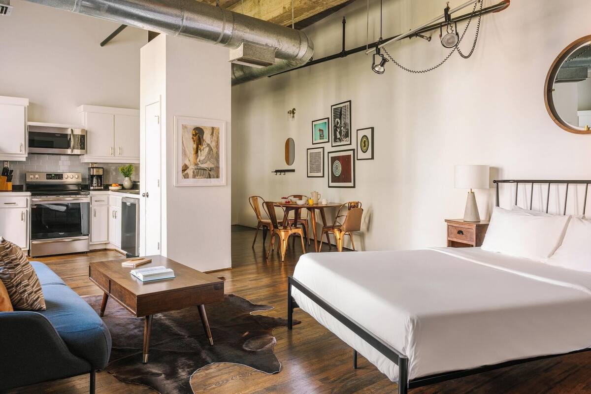 Ein modernes Hotelzimmer mit Bett, Schreibtisch, Essbereich und einer Küchenzeile.