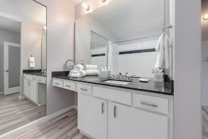 Un baño moderno con un espejo grande, muebles blancos, una encimera negra y una zona de ducha.