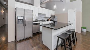 A modern kitchen with stainless steel appliances, a central island with stools, and a white backsplash.
