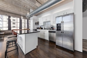 A modern kitchen with white cabinets, stainless steel appliances, and a bar area with stools. - Reside Houston Downtown A Wyndham Residence (Houston)