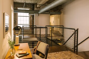 Ein Loft-Zimmer mit freiliegenden Lüftungsrohren, einer Wendeltreppe mit Metallgeländern, einem Holztisch mit einer Vase und einem Stuhl.
