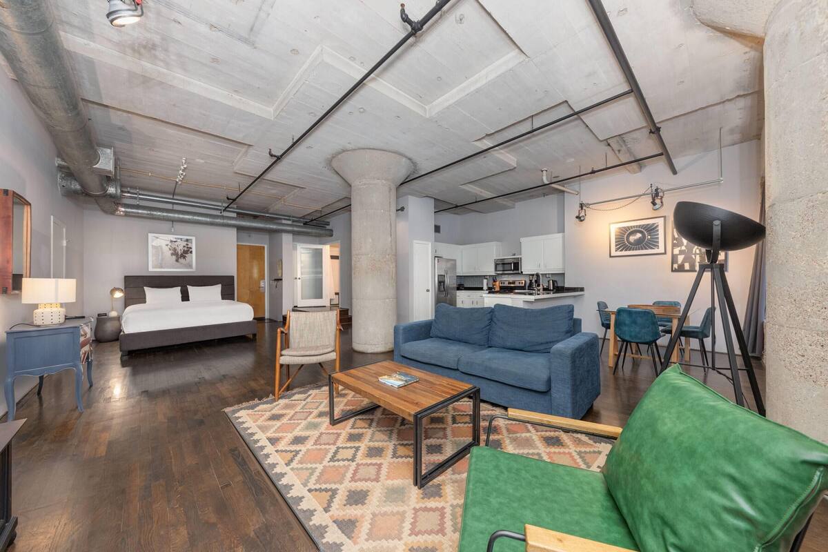 Ein modernes Apartment mit einem großen Bett, einem blauen Sofa, einem Couchtisch und einer Küchenzeile im Hintergrund.